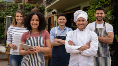 A group of five restaurant workers are standing together outside smiling.