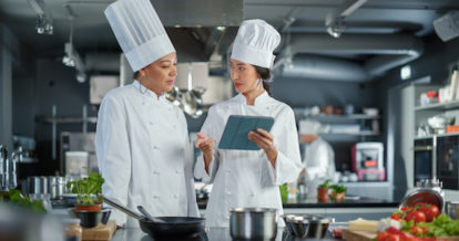 Two chefs talking in the kitchen with a tablet.