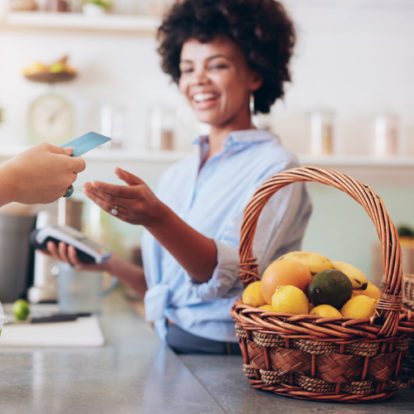 A customer handing their card to a female cashier, who has a payment terminal in their other hand.