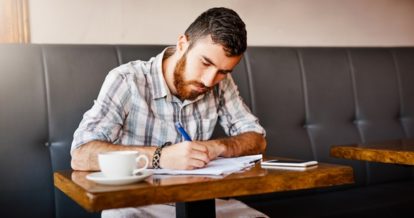 Man sitting in a restaurant booth while writing in a notebook.