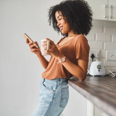 Woman leaning against a counter while holding a coffee cup and a phone