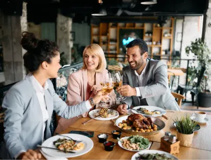 A group of happy coworkers drinking wine and enjoying a conversation over a meal at a restaurant.